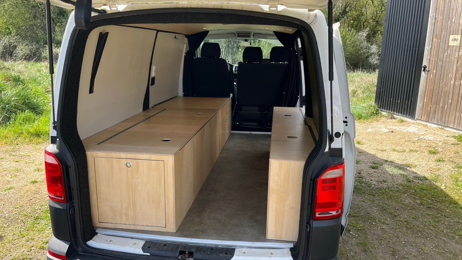 Volkswagen T6 aménagé avec deux meubles de rangement en bois sur mesure optimisant l’espace arrière du véhicule.